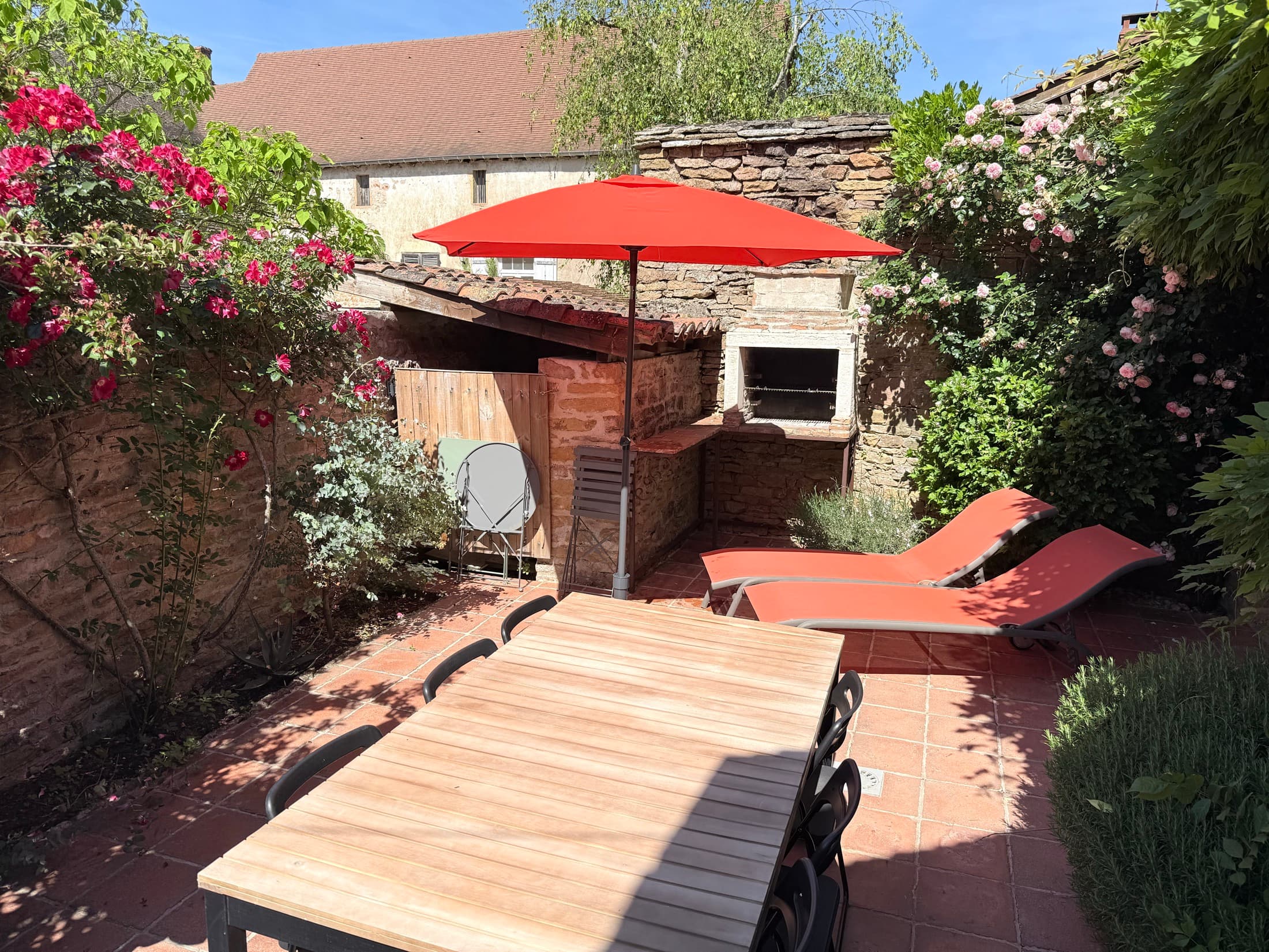 Terrasse fleurie avec table dressée, parasol et transats au soleil
